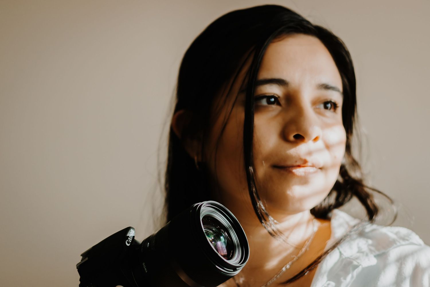A photographer holds their camera while posing against a neutral background.