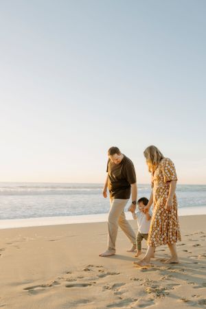 Family walking together on sandy beach at sunset leaving footprints behind.
