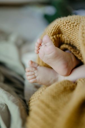 Close-up of tiny baby feet wrapped in a cozy knit blanket.