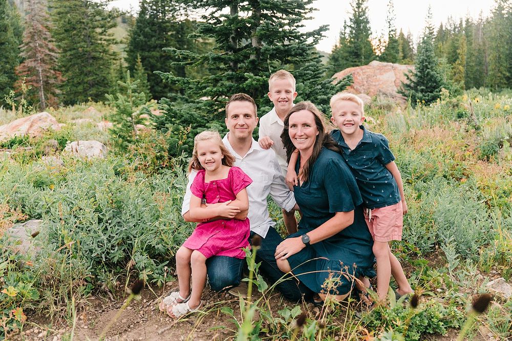 A casual family portrait in a mountain setting with evergreens and wildflowers.