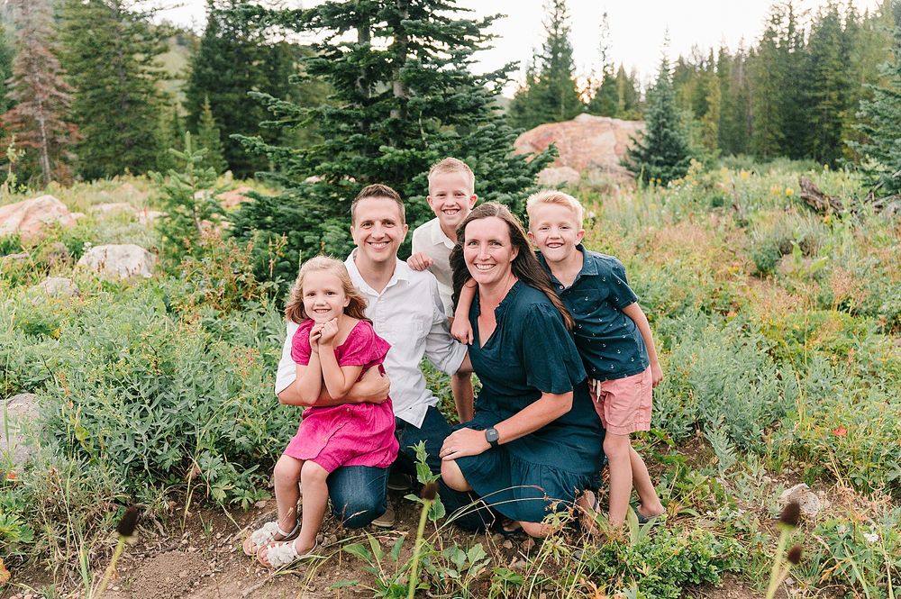 A cheerful family group portrait in a mountain wilderness setting with evergreen trees.