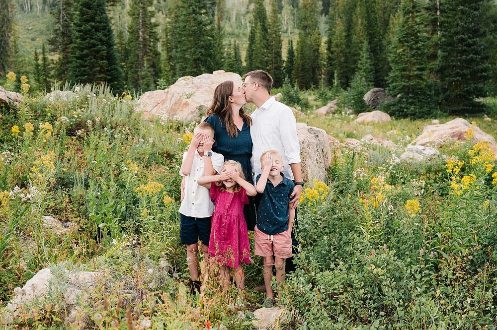 Family portrait among wildflowers and pine trees in a scenic mountain setting.