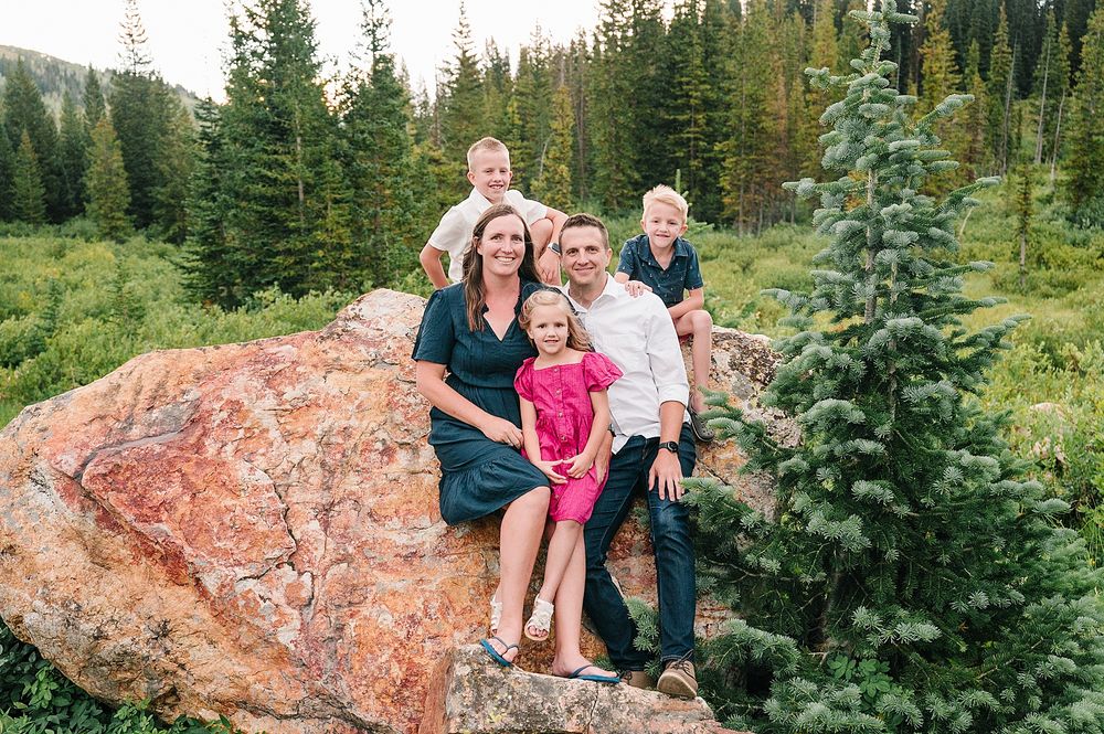 Family group photo on a large red boulder with evergreen forest backdrop in mountain setting.