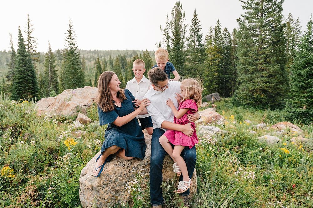 Happy group enjoying outdoor portraits on large boulders surrounded by evergreen trees and wildflowers in mountain setting.