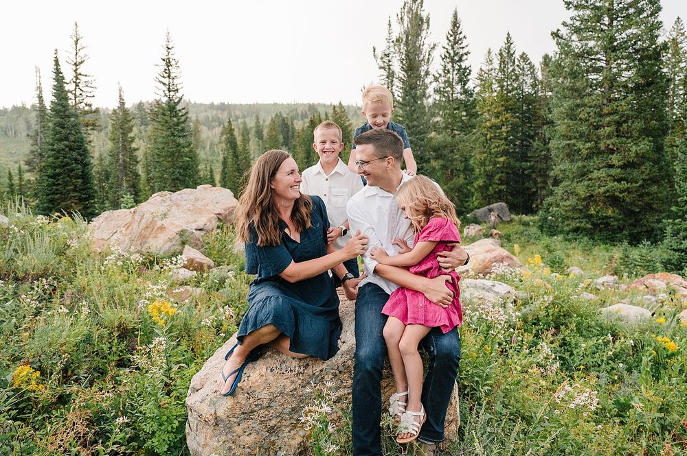 Casual outdoor portrait session on large boulder with mountain vista and pine forest background.