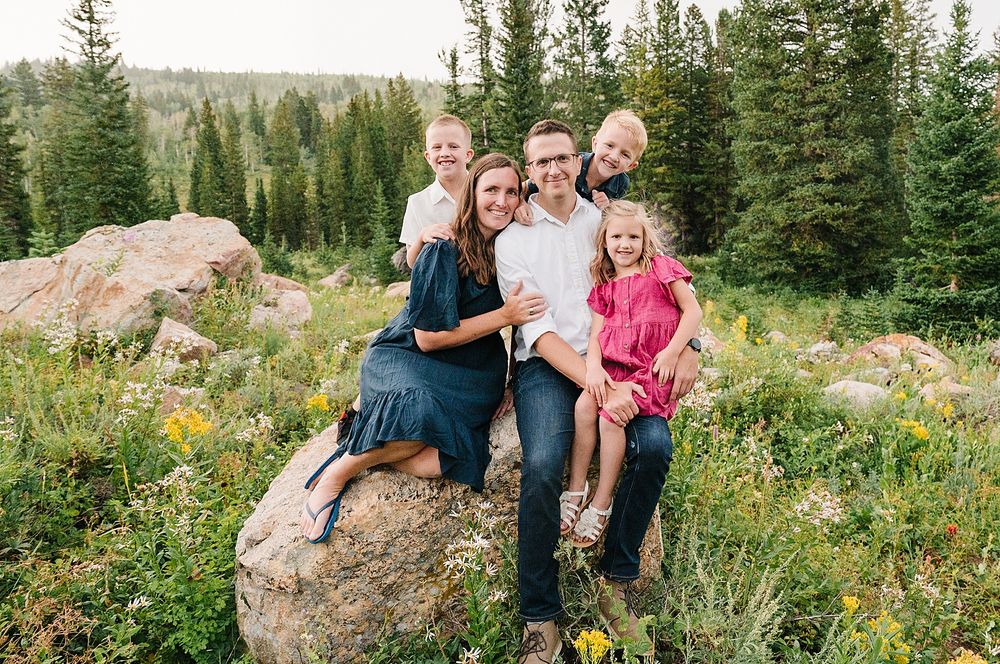 Relaxed group portrait on rocky outcrop surrounded by mountain wilderness and evergreen trees.