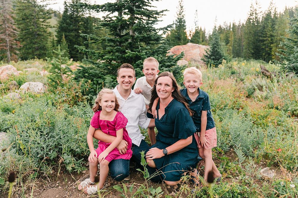 A family portrait in a mountain meadow surrounded by evergreen trees and wildflowers.