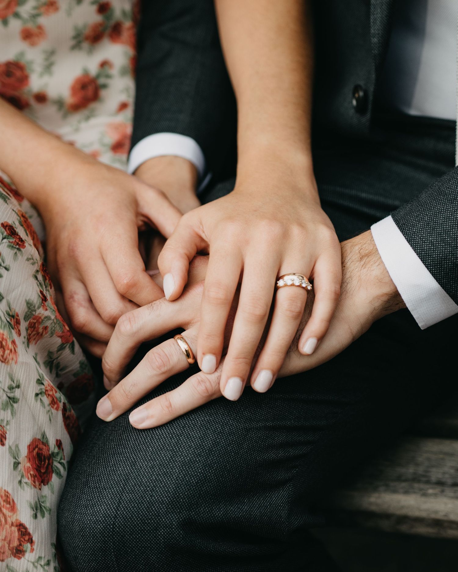 Newlywed couple holding hands showing wedding rings, bride wearing floral dress and groom in suit.