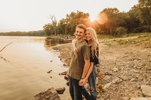 Couple stands together on rocky shoreline during sunset.