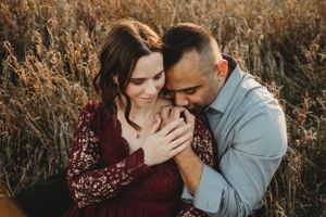 Romantic couple embraces in a golden field of tall grass during sunset.