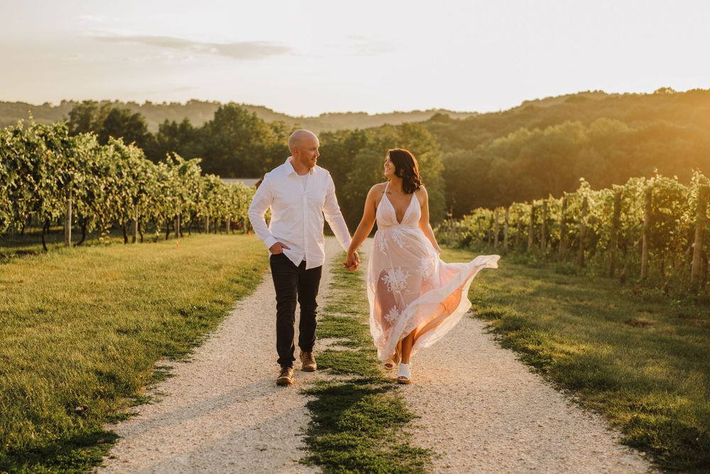 A couple walking hand in hand through a vineyard at sunset with flowing dress and golden light.