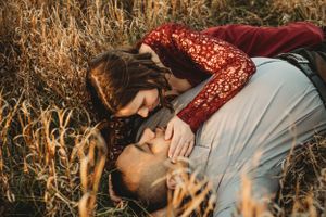 Intimate moment shared between couple lying in autumn field wearing burgundy and blue.