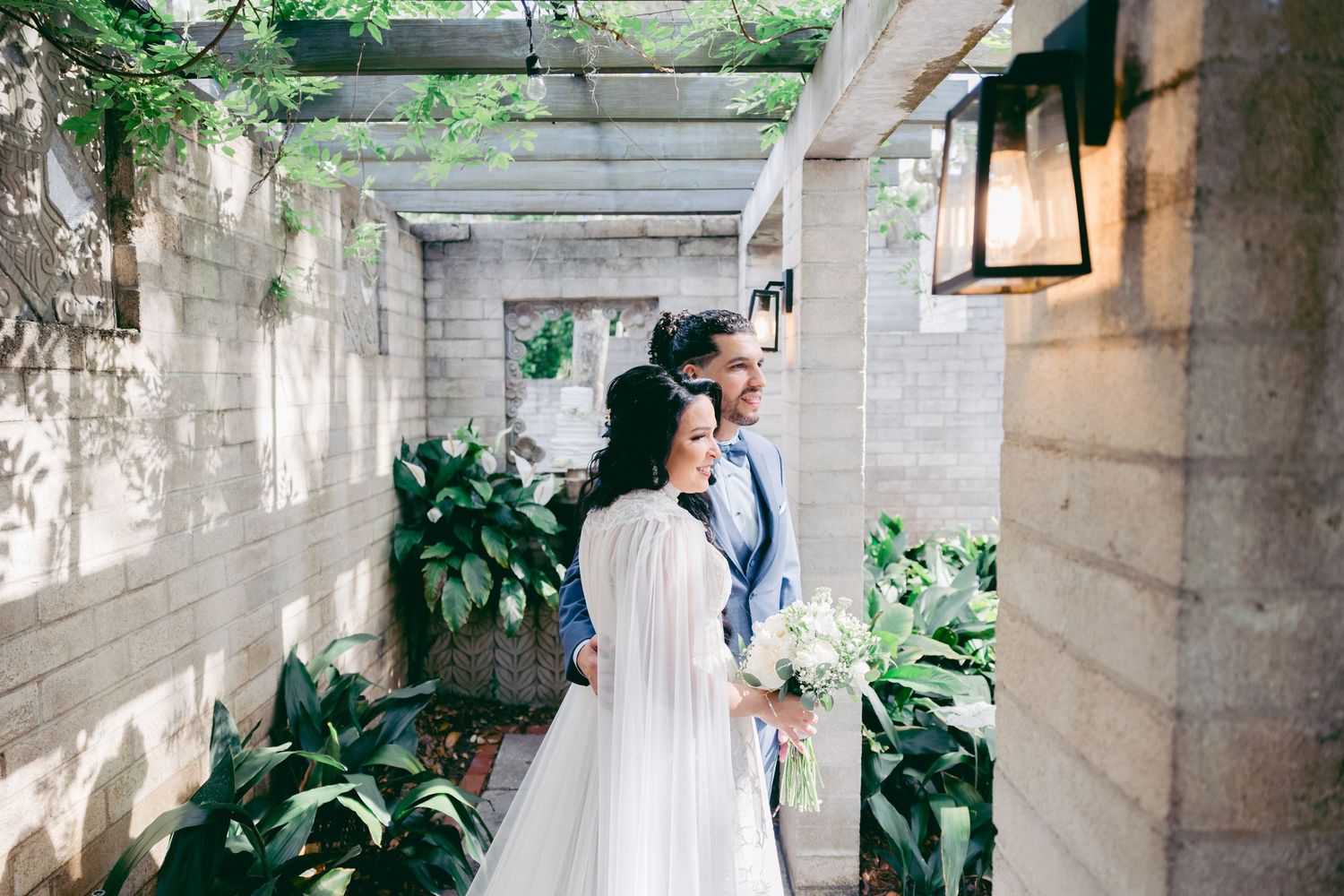 Couple sharing an intimate moment in a garden walkway with white pergola and greenery.