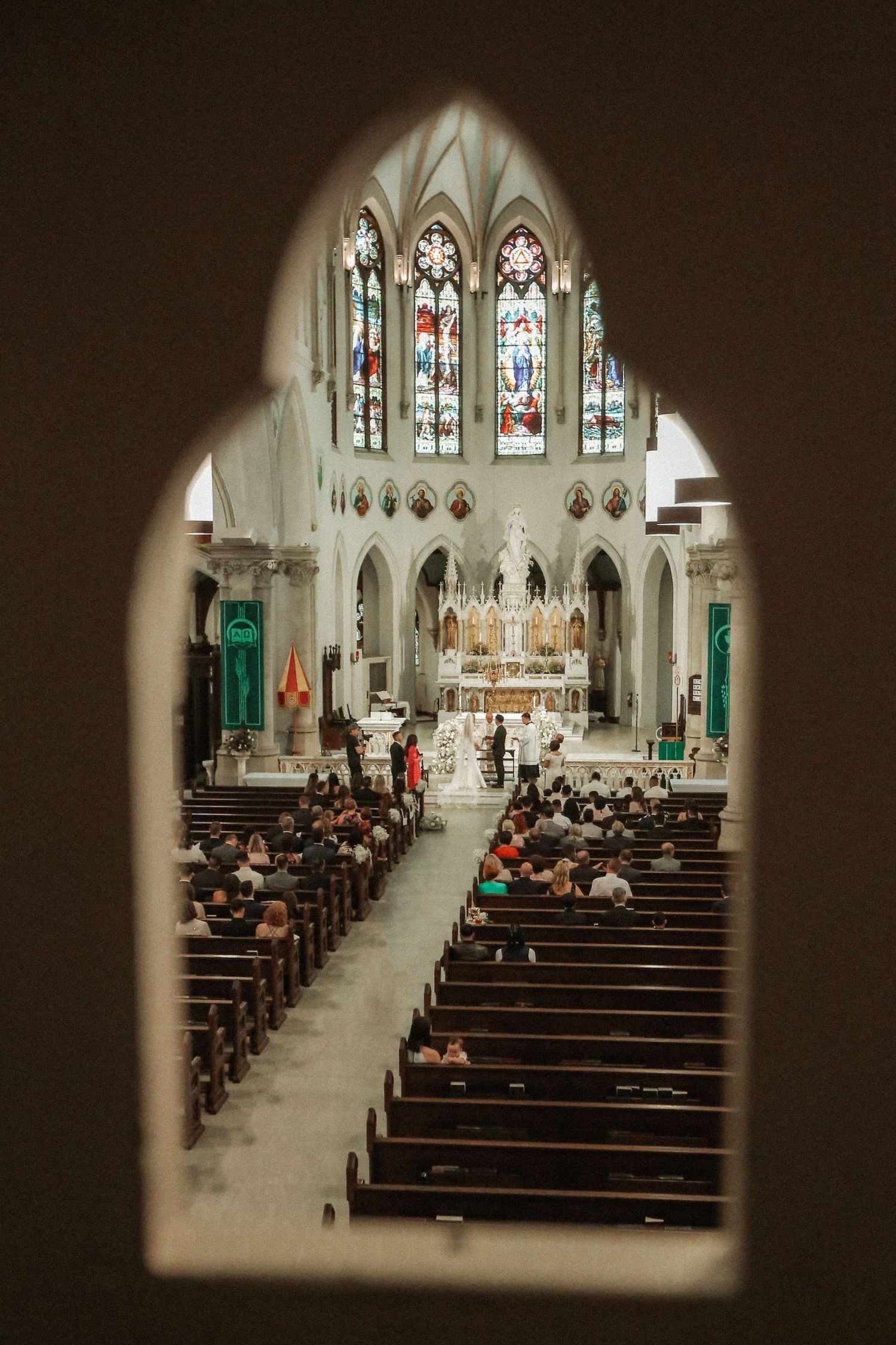 Interior view of a Gothic cathedral during a ceremony with stained glass windows and filled pews.