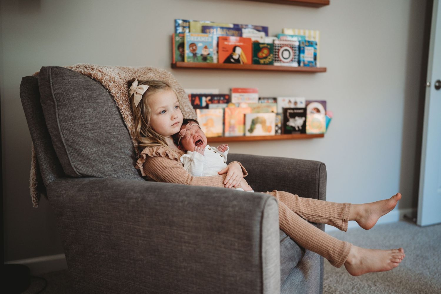Playful moments captured on a grey couch with book shelves mounted on the wall in background.
