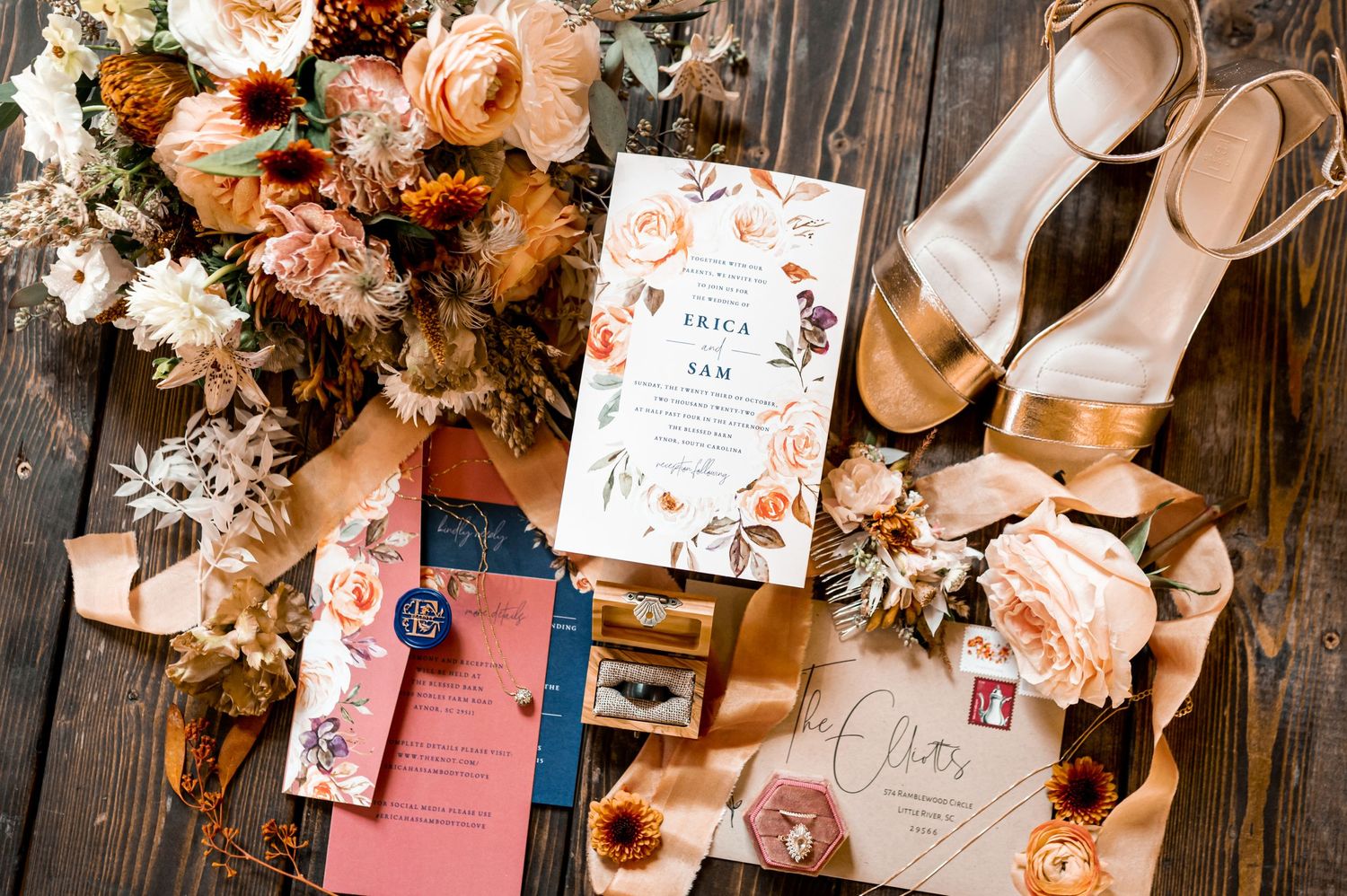 Wedding details including floral arrangements and stationery laid out on rustic wooden surface.