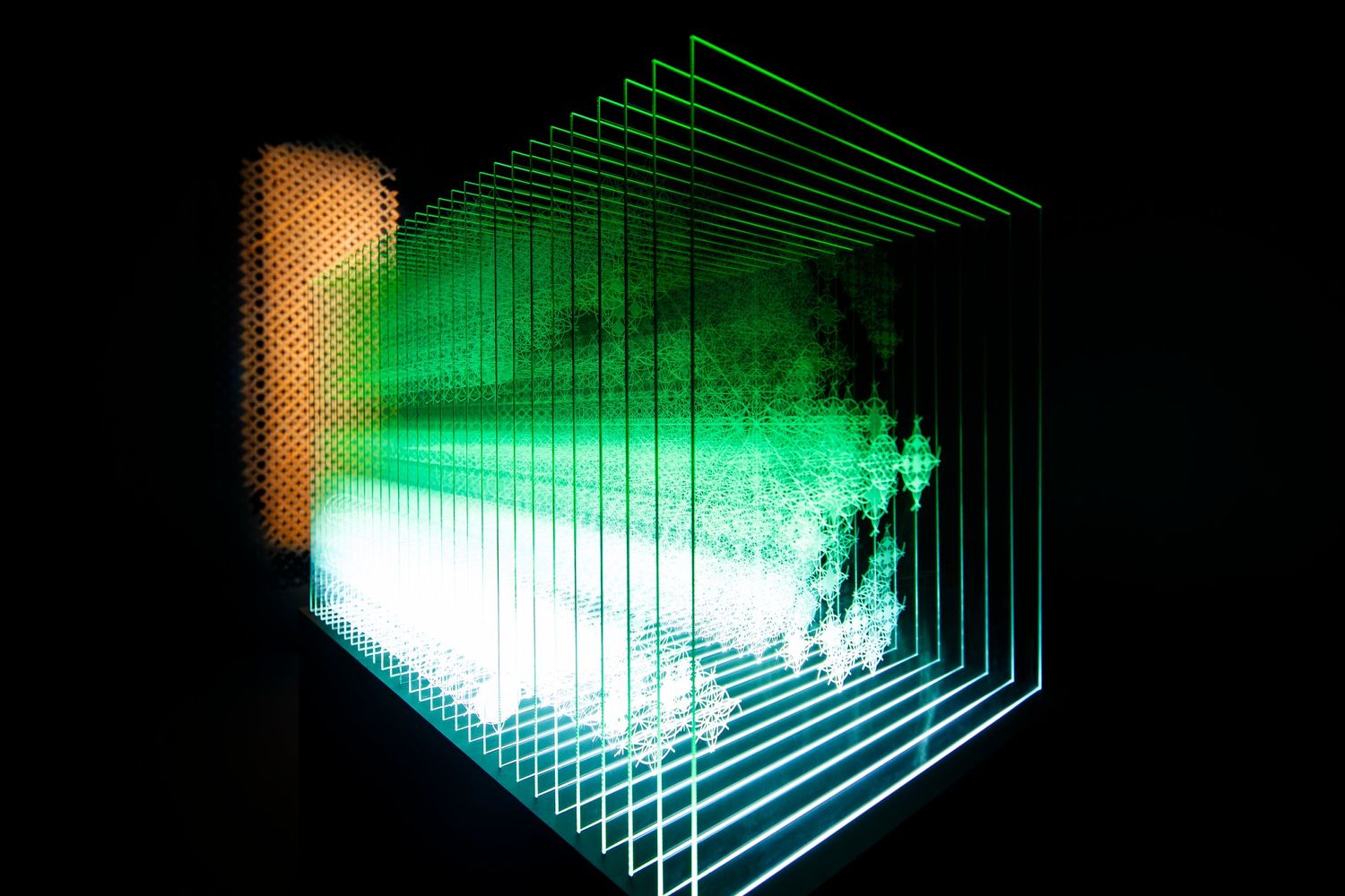 Layered glass panels create a glowing green geometric light installation against a dark background.