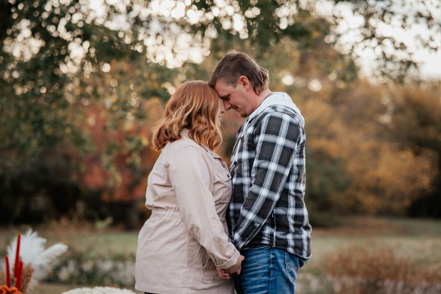 A romantic fall engagement photo of a couple in casual attire sharing an intimate moment outdoors.