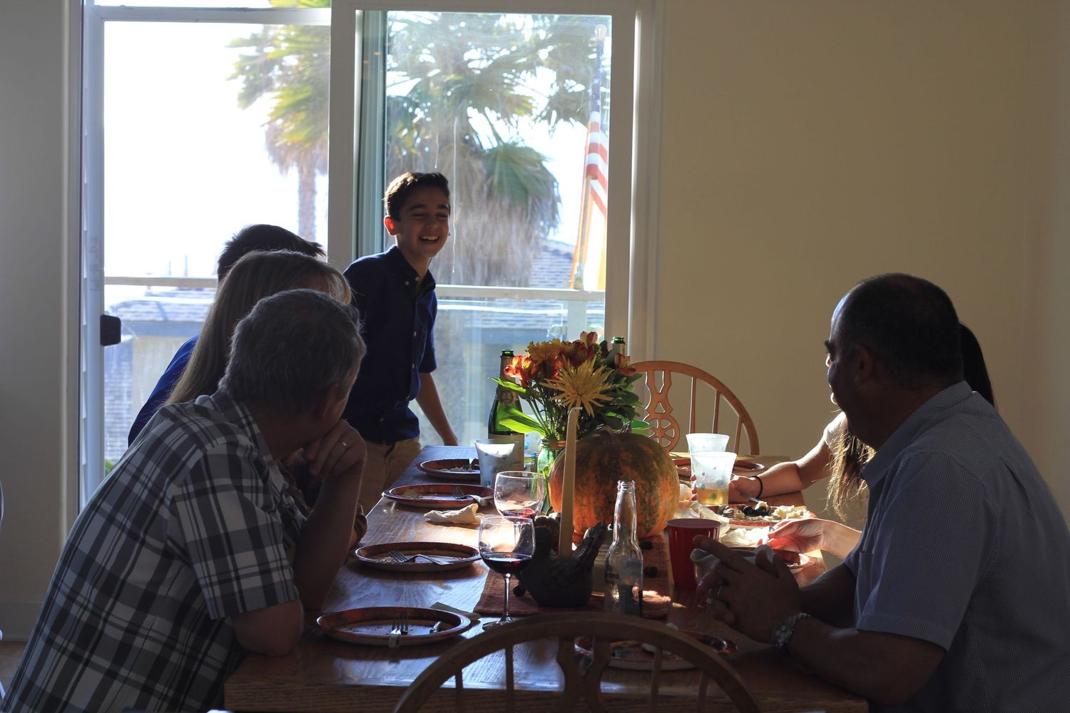 A group gathers around a dining table with flowers and sunlight streaming through windows.