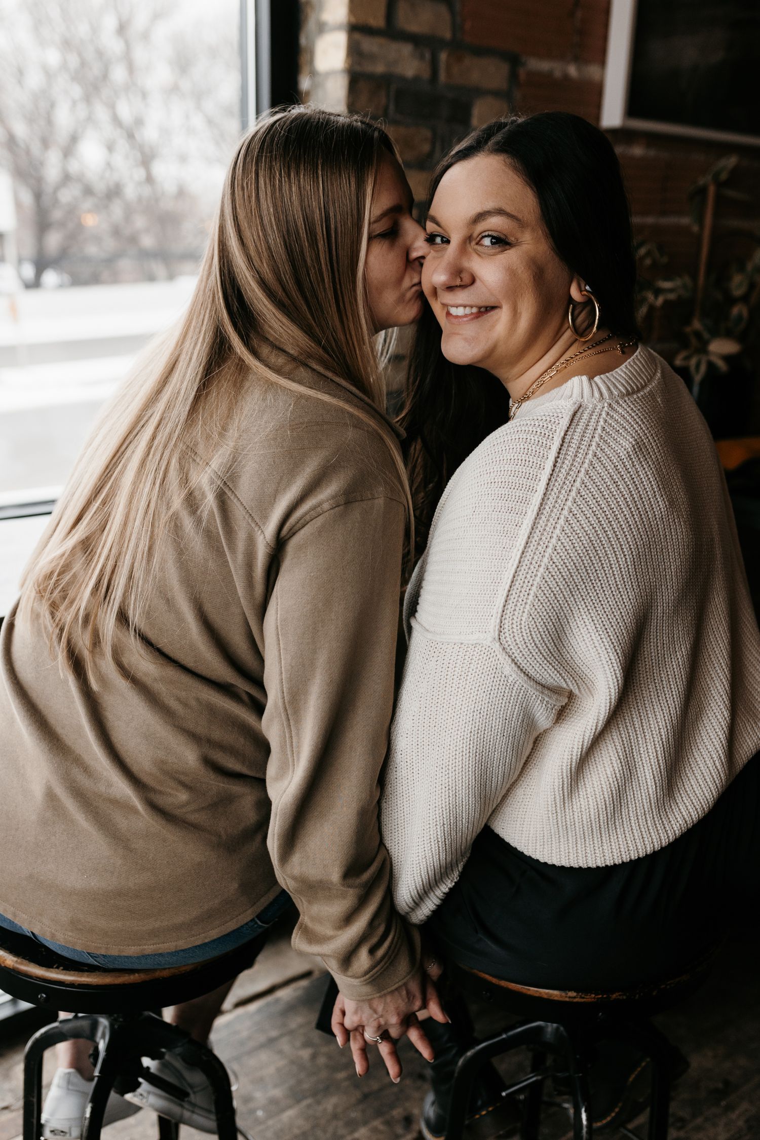 Two friends sharing an intimate moment at a cafe with brick walls and natural lighting.