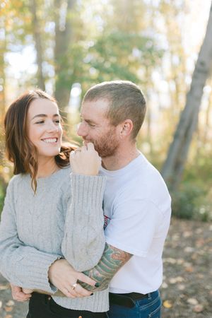 Couple sharing intimate moment outdoors with autumn trees in background.