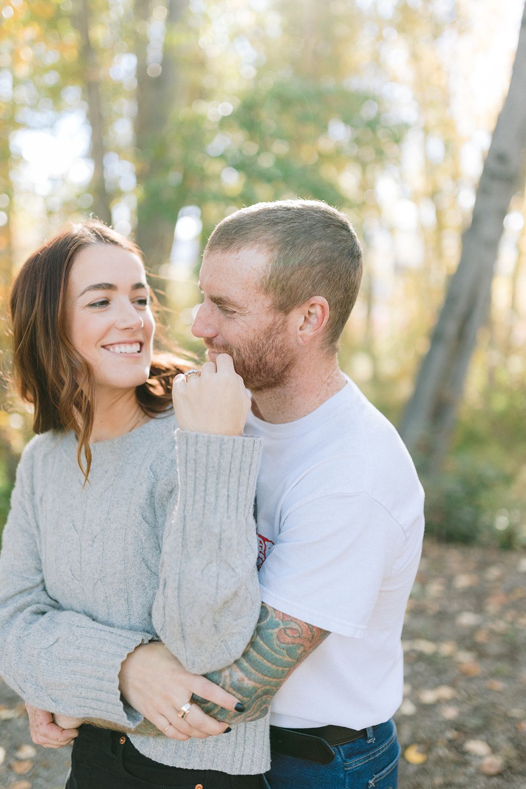 Couple sharing intimate moment outdoors with autumn trees in background.