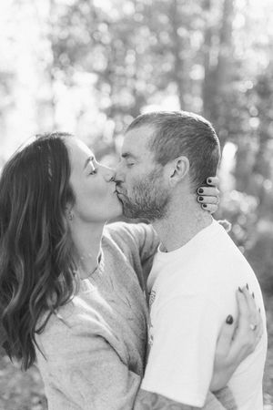 Black and white portrait of couple sharing romantic kiss in forest setting.