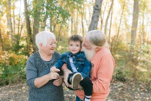 A heartwarming autumn outdoor scene with three generations sharing a joyful moment together in a wooded setting.
