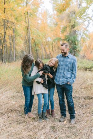 A family of four sharing a laugh together in a fall forest setting with golden leaves.