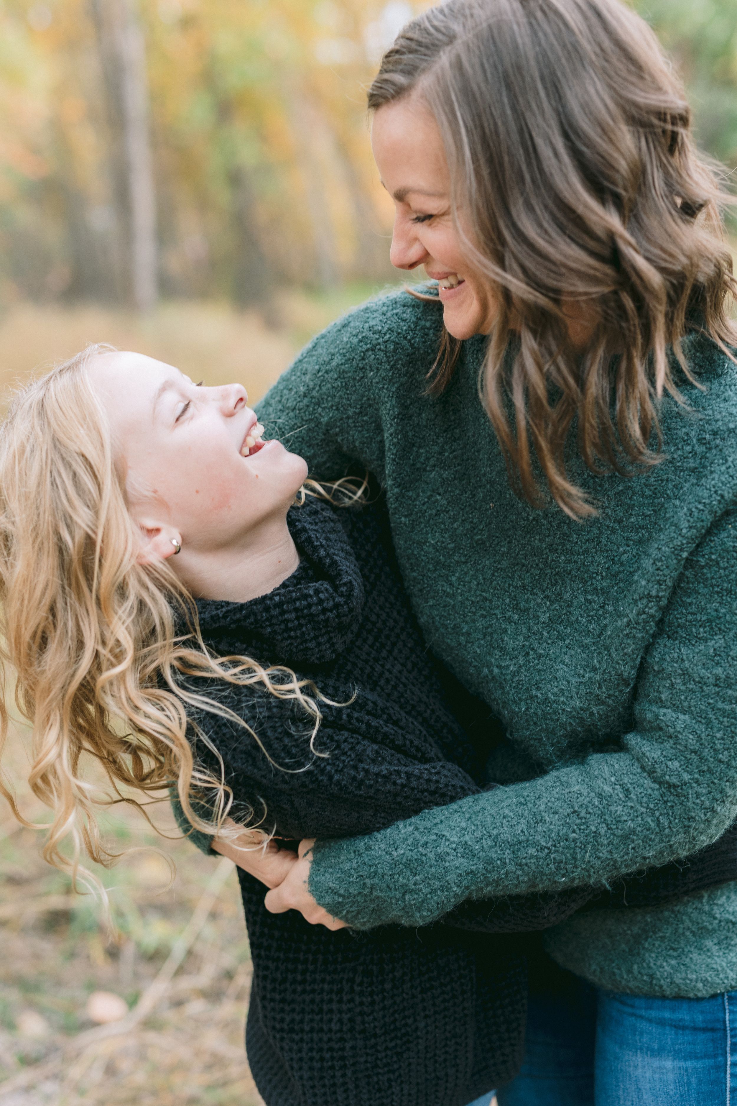 Two people share a joyful laughing moment together against a backdrop of fall trees.