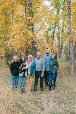 A group of six people standing together for a family portrait in an autumn forest setting.