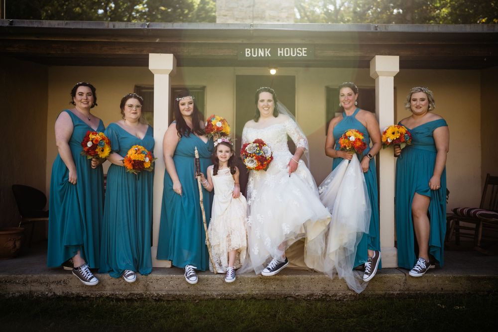 Wedding party in teal dresses posing in front of a brown building.