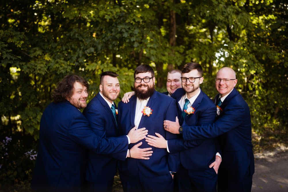 Groomsmen in navy suits hugging and laughing together outdoors.