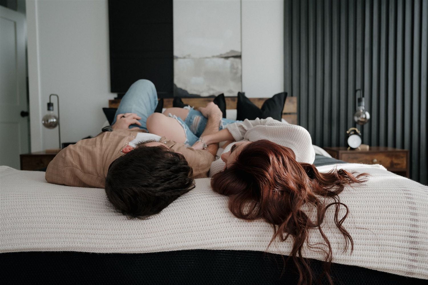A couple lying on bed together in casual attire in modern bedroom setting.