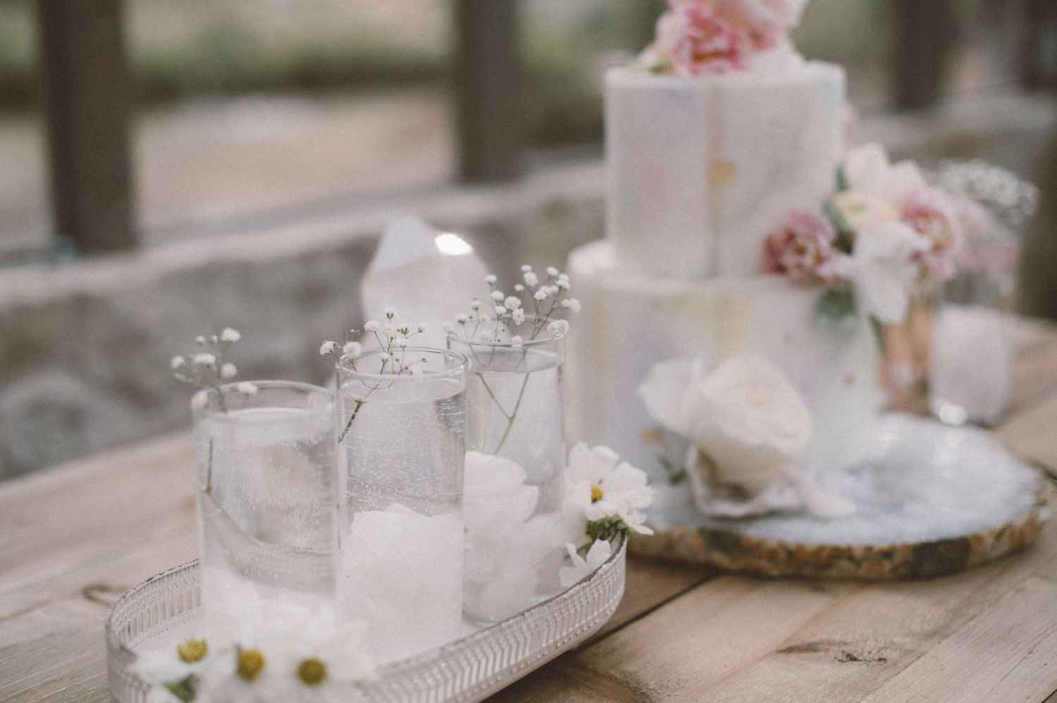 Minimalist wedding decor with glass bottles and delicate floral arrangements on rustic table.