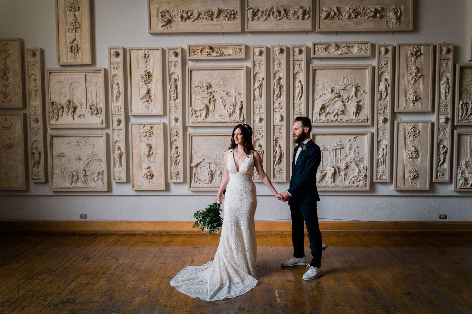 Wedding couple posing in formal attire against a wall of vintage decorative panels.