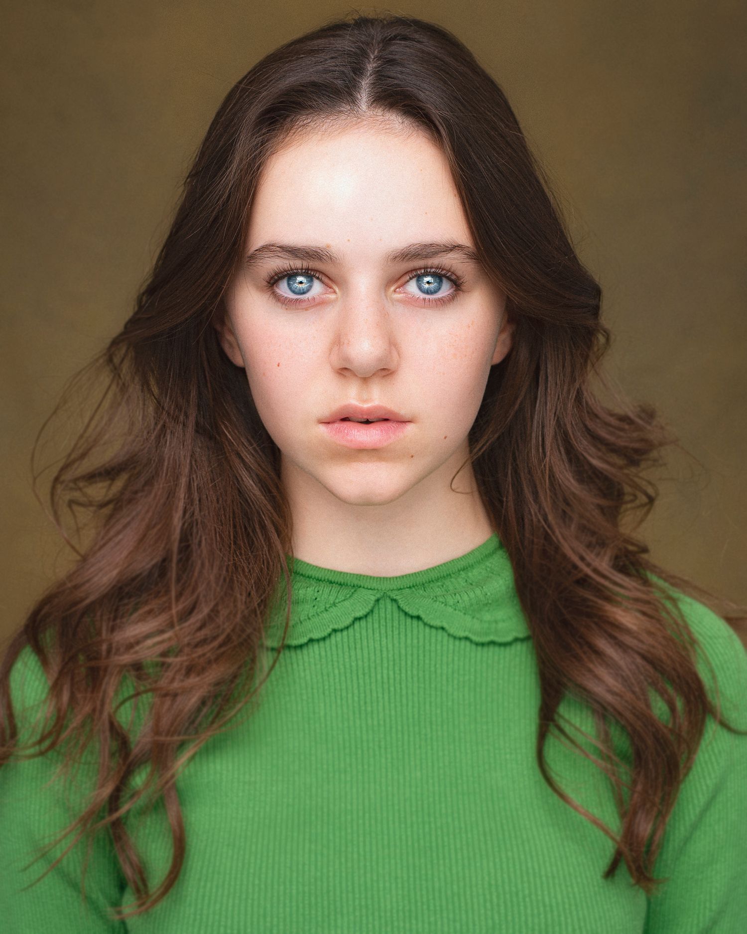 Portrait of a young woman in green collar sweater with striking blue eyes and long brown hair.