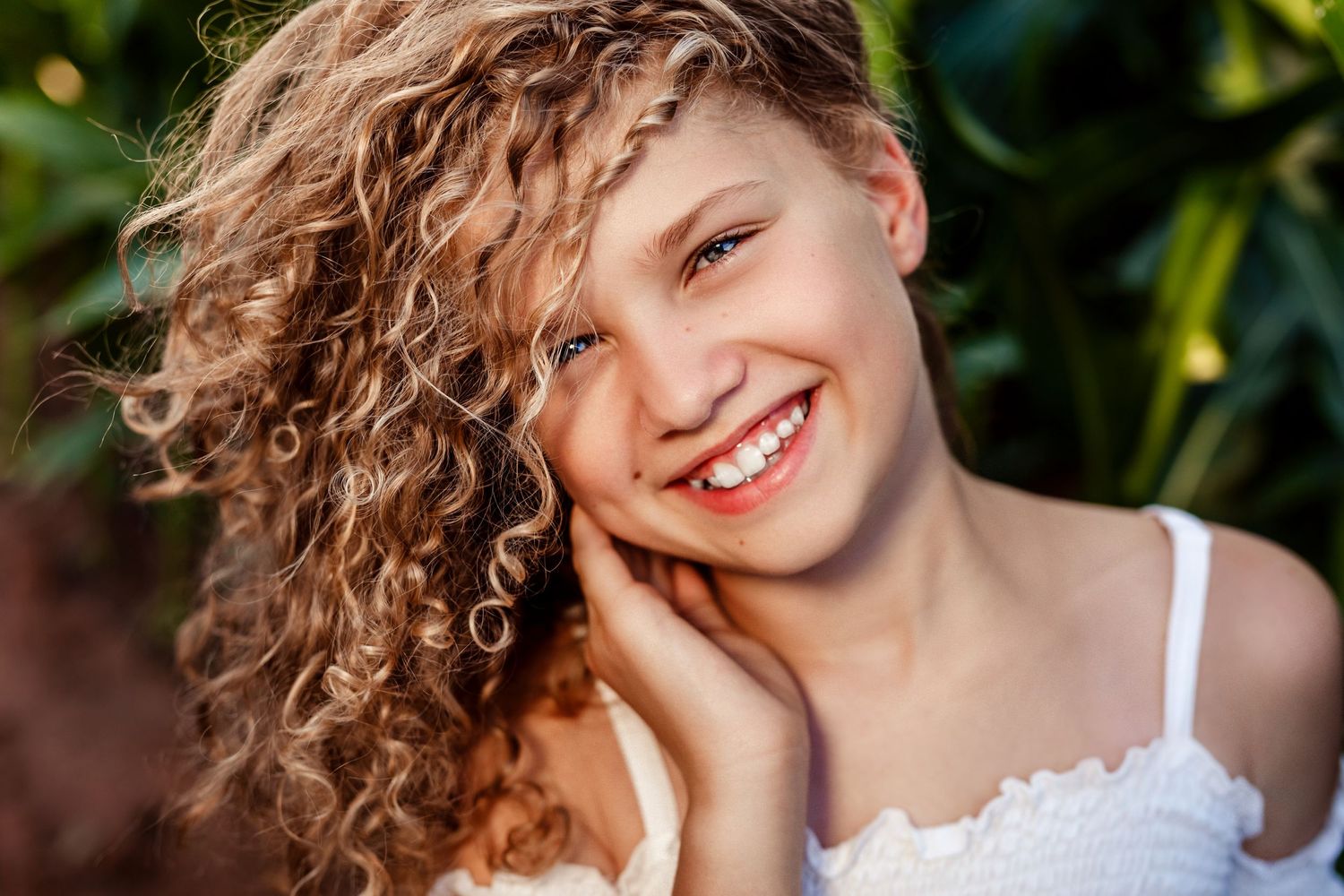 Natural beauty portrait featuring curly hair and bright smile in sunlit garden setting.