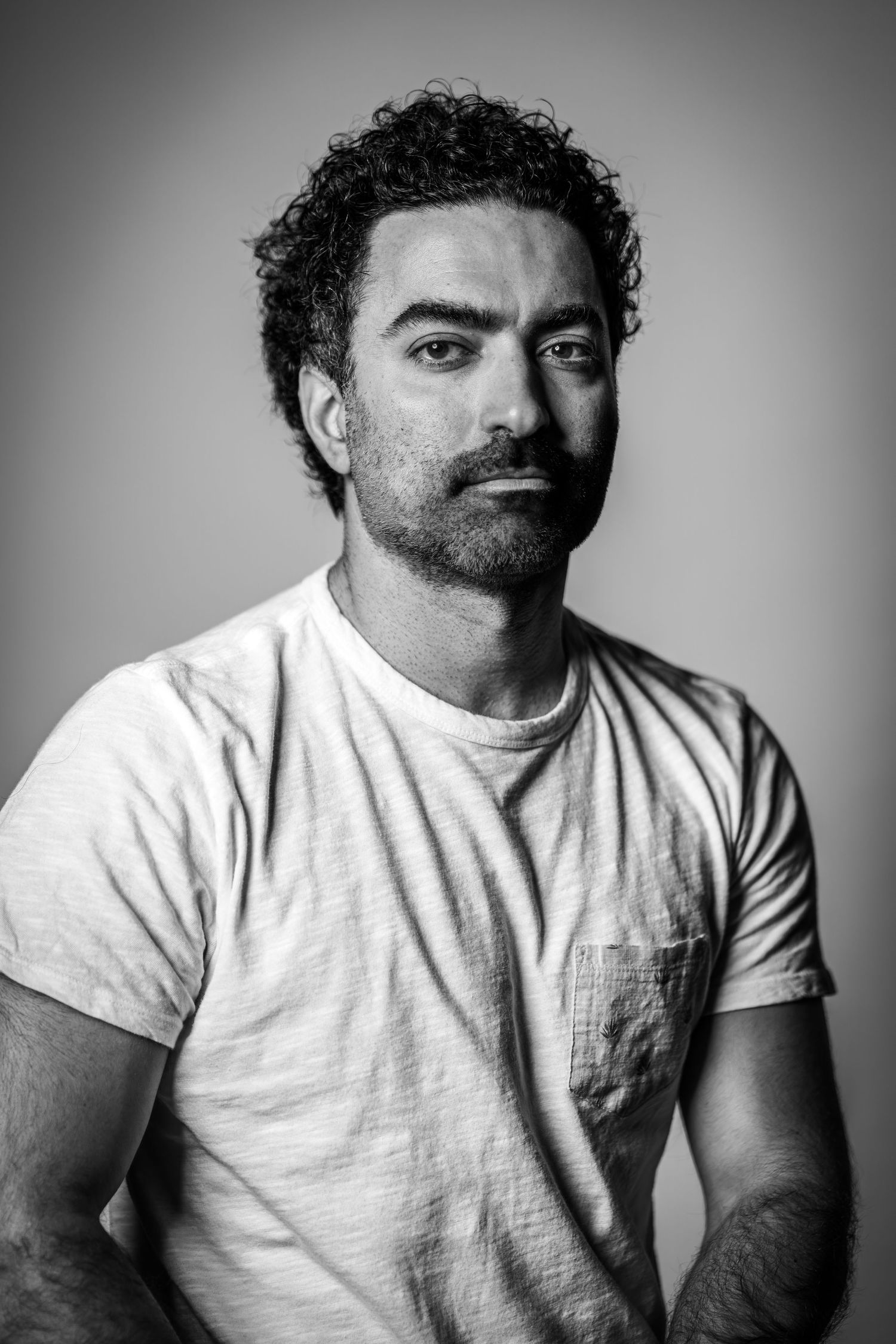 Black and white portrait of a man in a white t-shirt against a neutral background.