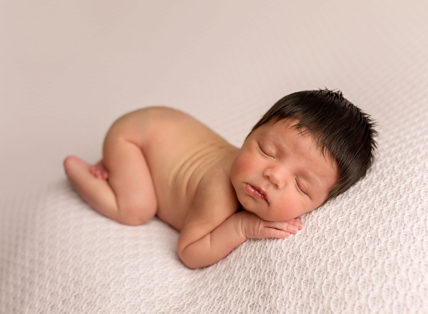 Peaceful sleeping newborn baby curled up on white textured backdrop.