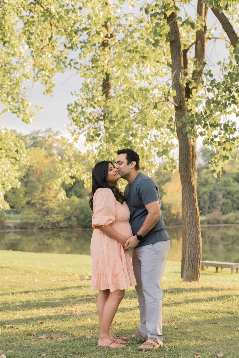 pregnant couple wearing pink and blue kissing at a park in troy michigan
