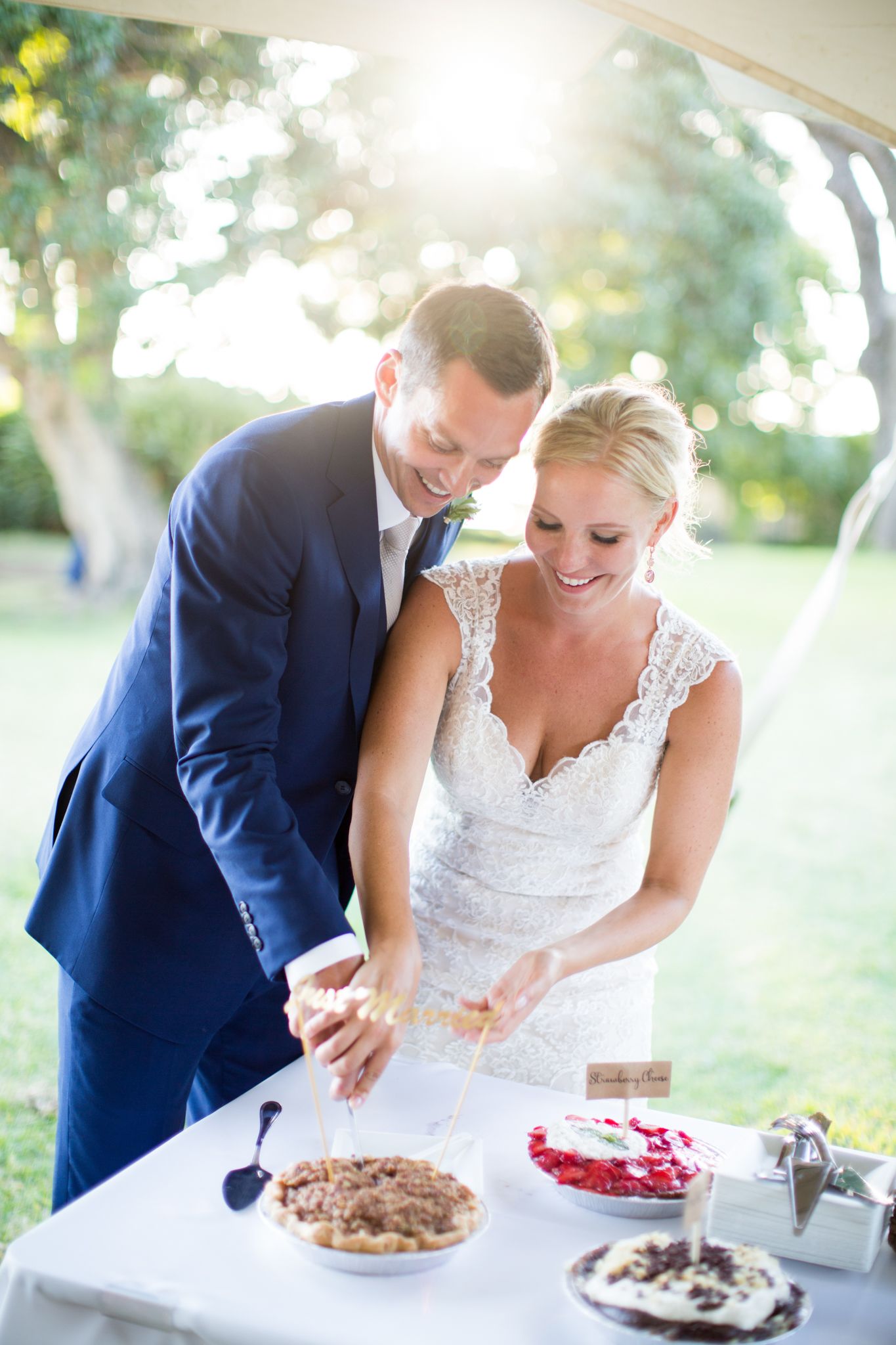 Wedding couple shares a laugh while cutting dessert at their outdoor reception.