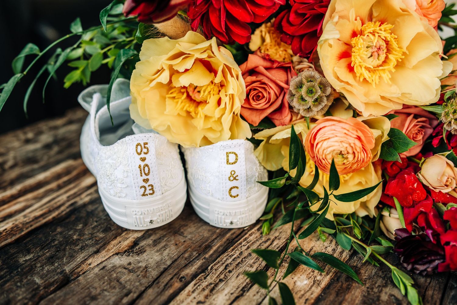 White baby shoes surrounded by colorful roses on wooden surface.