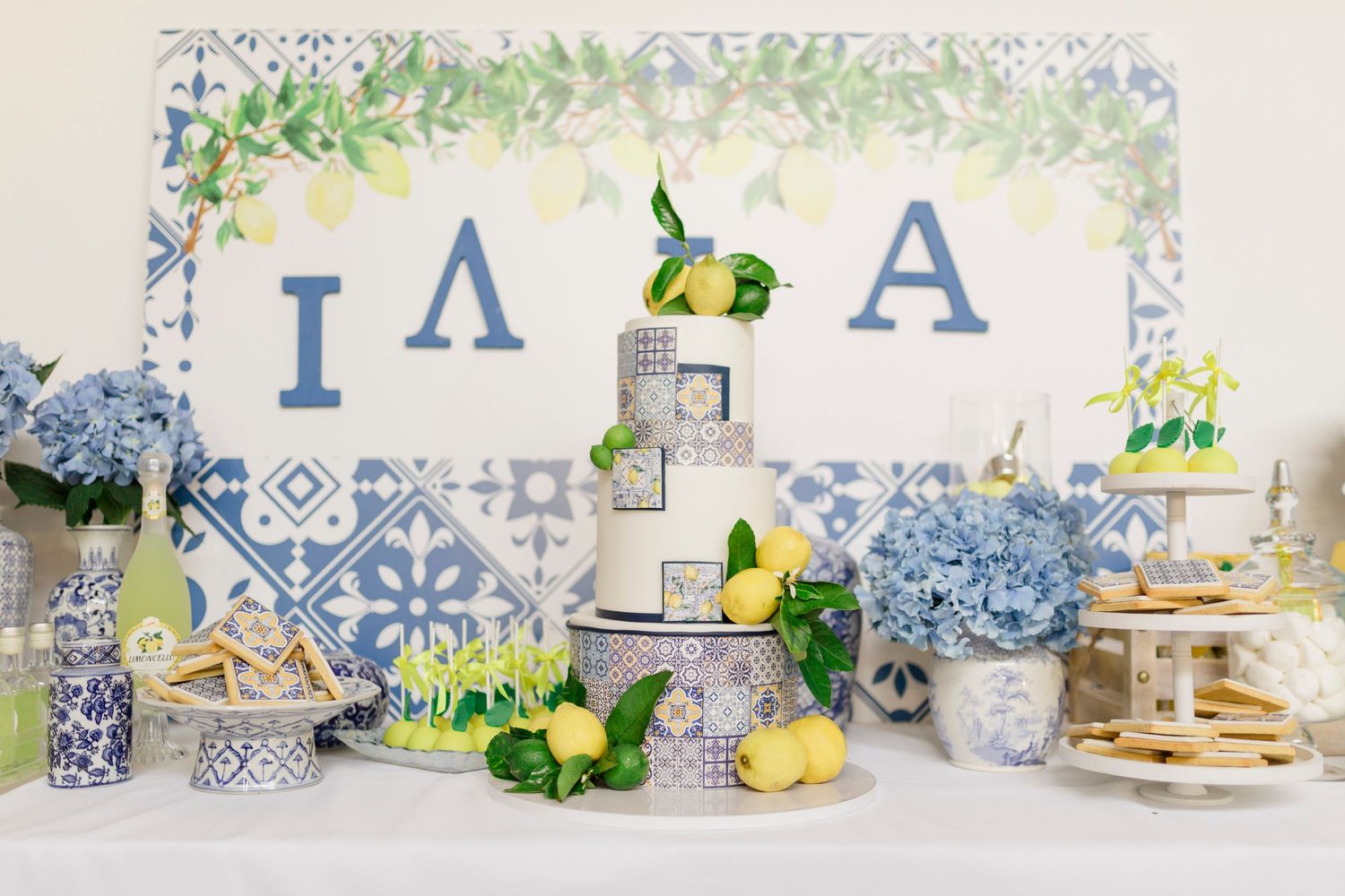 Dessert table with blue and white decorations, flowers, and lemon accents.