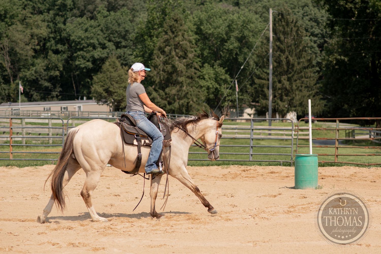 Rider practicing horsemanship in sandy arena with blue barrel obstacle.