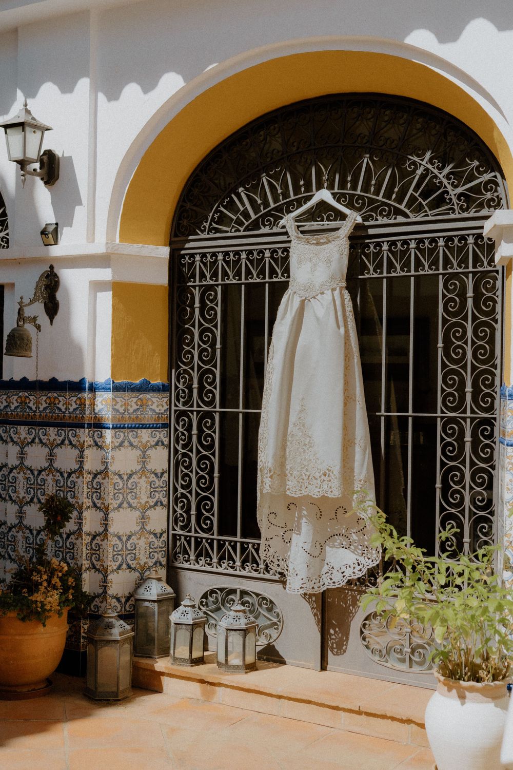 A white wedding dress hangs in an ornate archway with decorative ironwork and lanterns on display. Destination Wedding in Malaga, Spain.