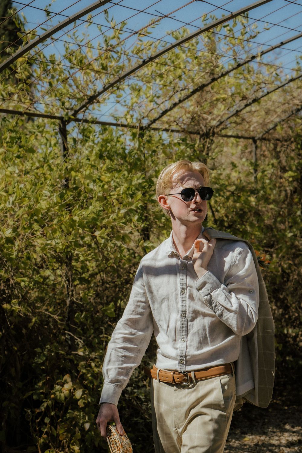 Groom in light colored outfit walking through a garden arch. Destination Wedding in Malaga, Spain.