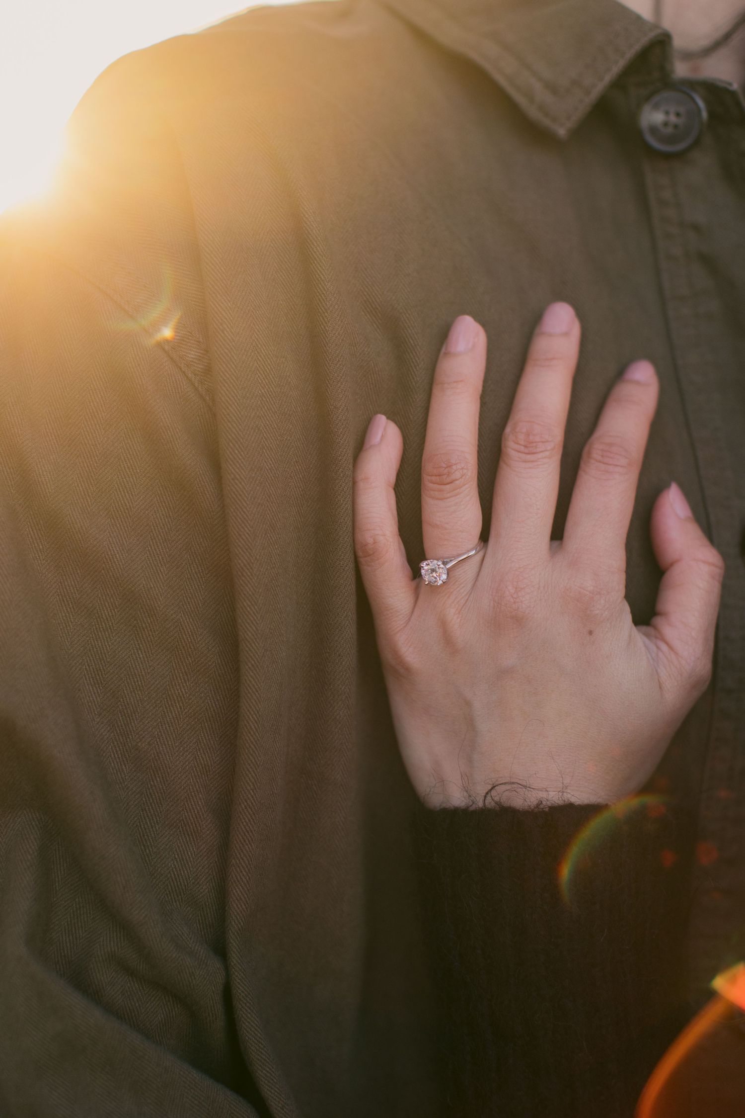 Close-up of hands with engagement ring glowing in warm sunset light.