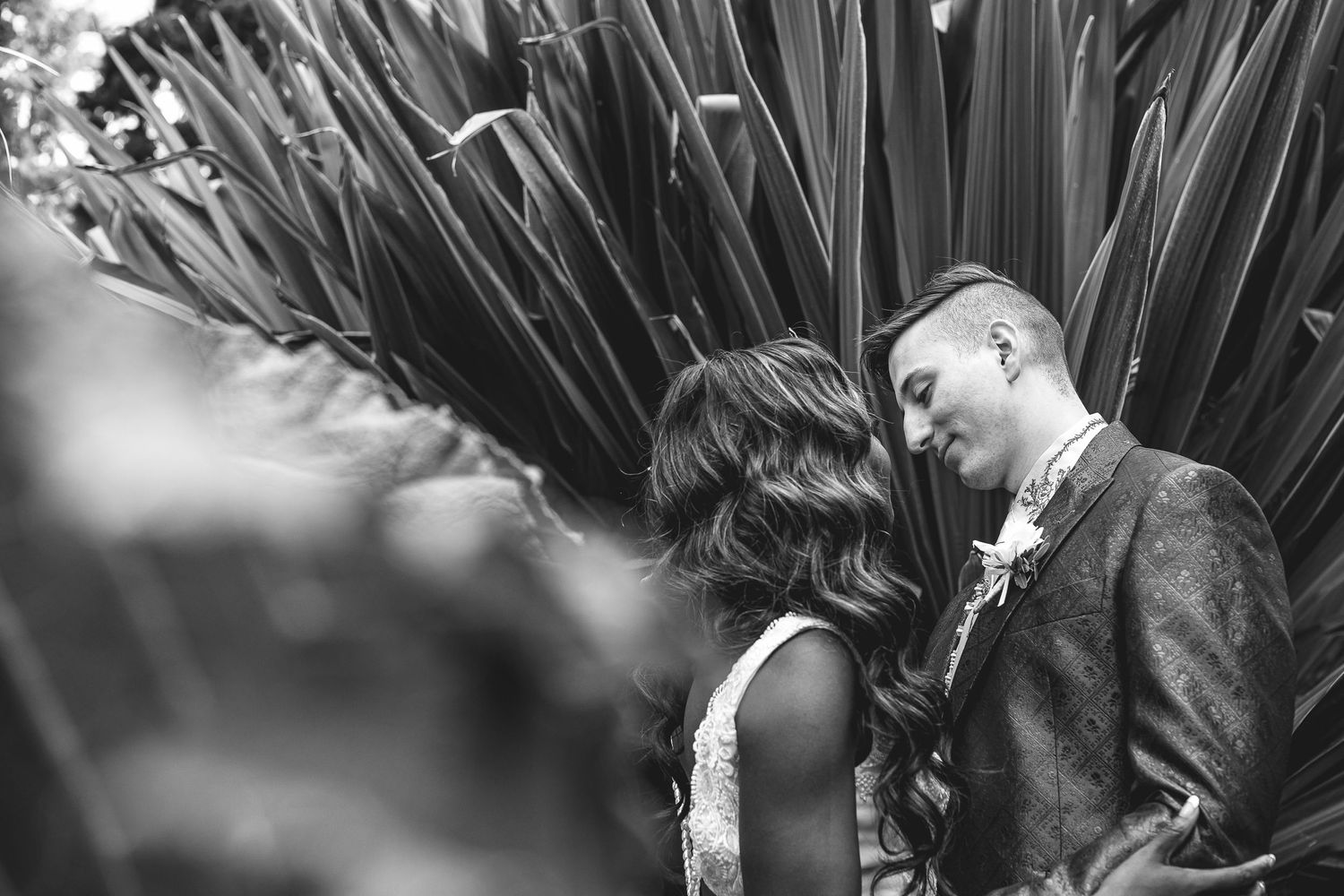 Intimate black and white garden portrait of a romantic couple among tall leaves.