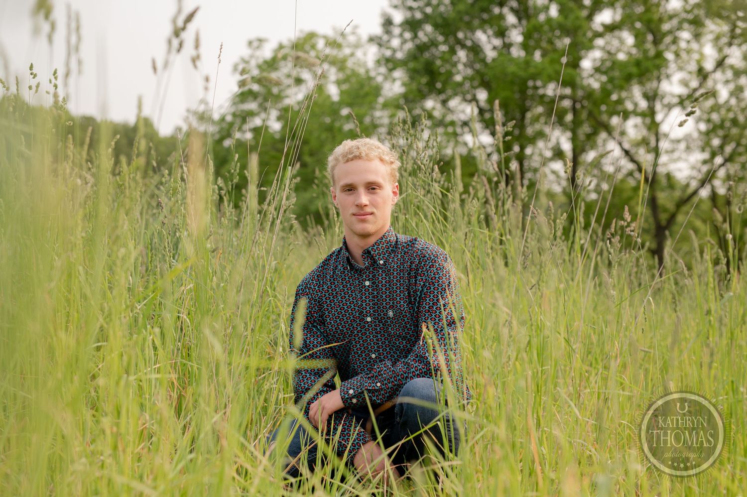 Portrait framed by tall summer grasses with trees visible in distance.